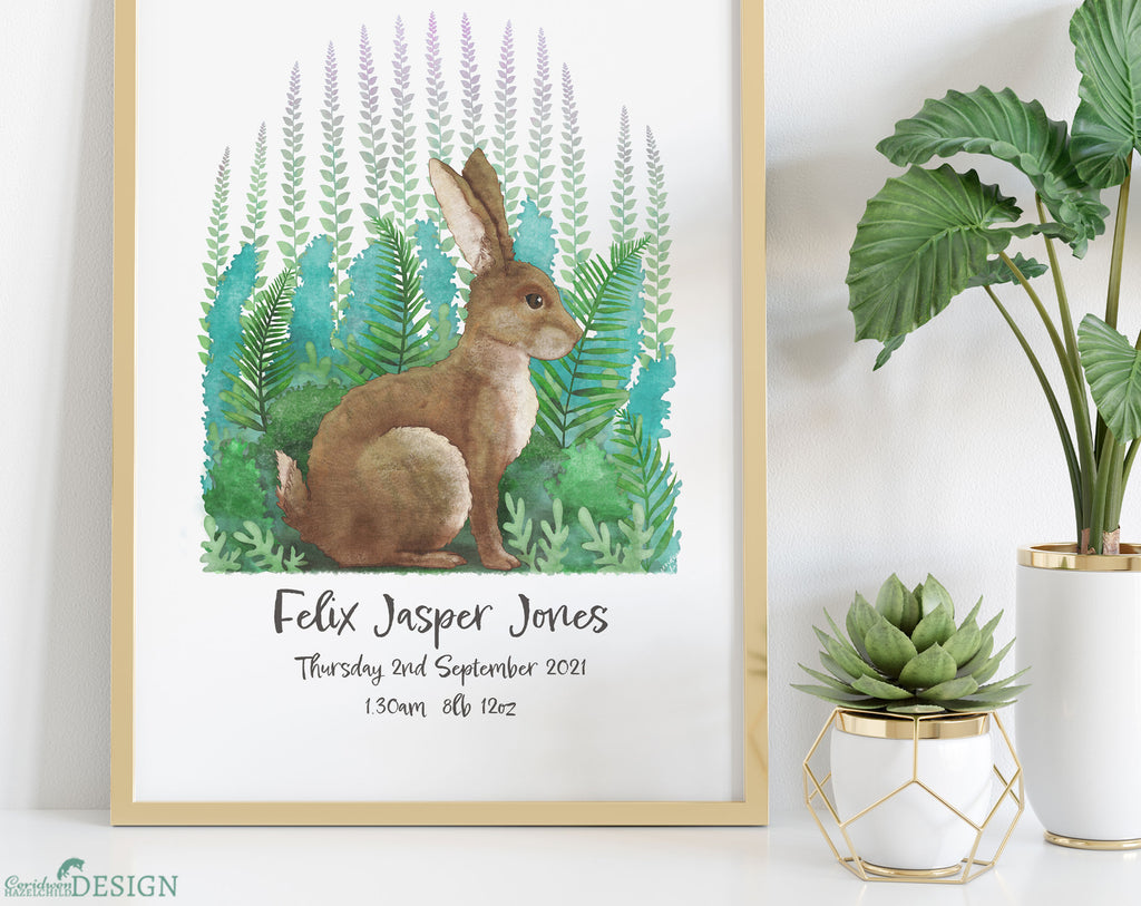 A framed illustration of a rabbit by Ceridwen Hazelchild, personalised with a baby boy's name and birth details, placed on a shelf and surrounded by plants.
