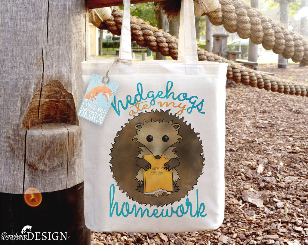 A tote bag with a print of a hedgehog holdinga book, surrounded by the text "Hedgehogs Ate My Homework".