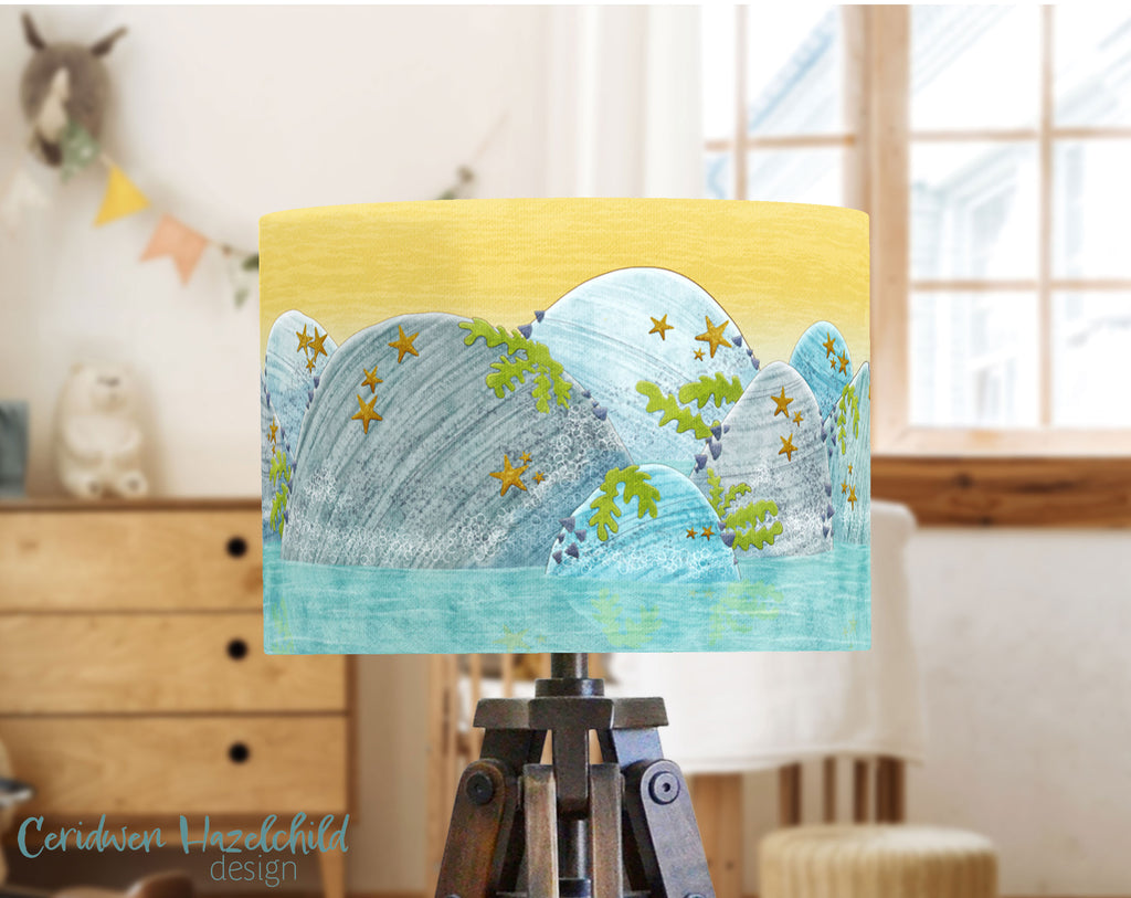 Rockpool lampshade by Ceridwen Hazelchild on a lamp base in a bright children’s nursery, with large windows and colourful bunting in the background.