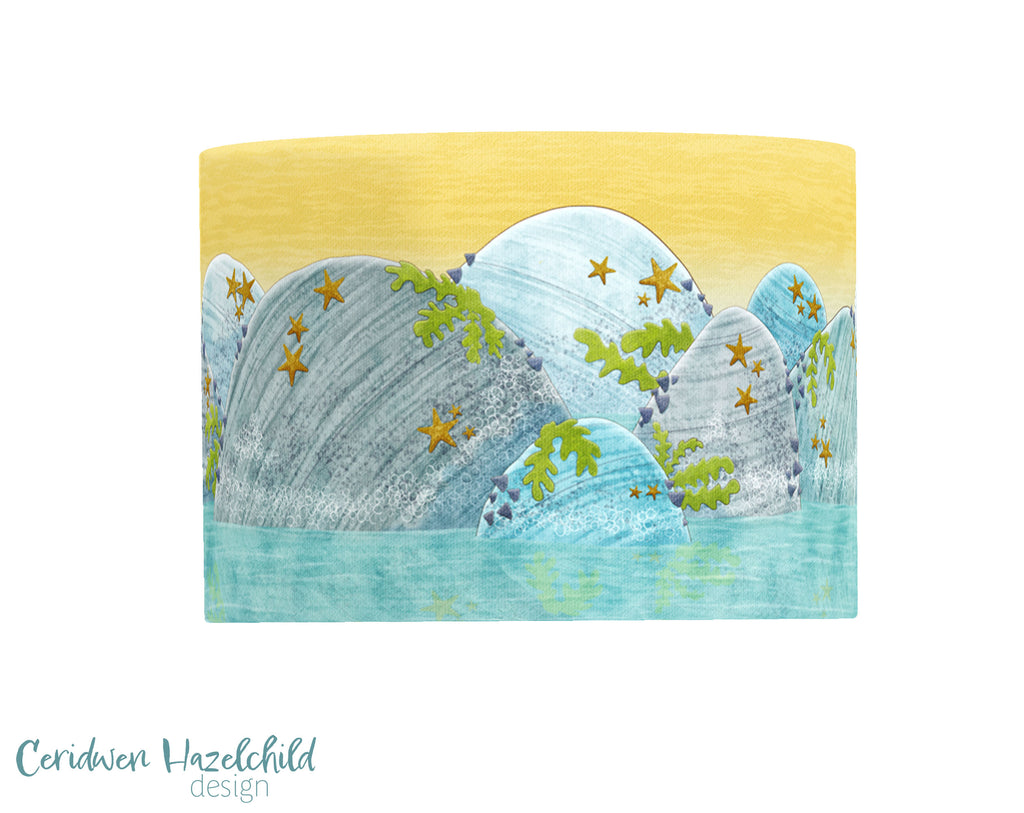 Rockpool lampshade by Ceridwen Hazelchild – handmade drum lampshade featuring coastal illustrations of seaweed, rocks, crabs, and fish on a soft ocean-toned background.