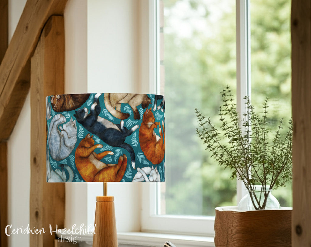 Lamp with a colorful cat design in front of a window with a plant on a windowsill in a country home.