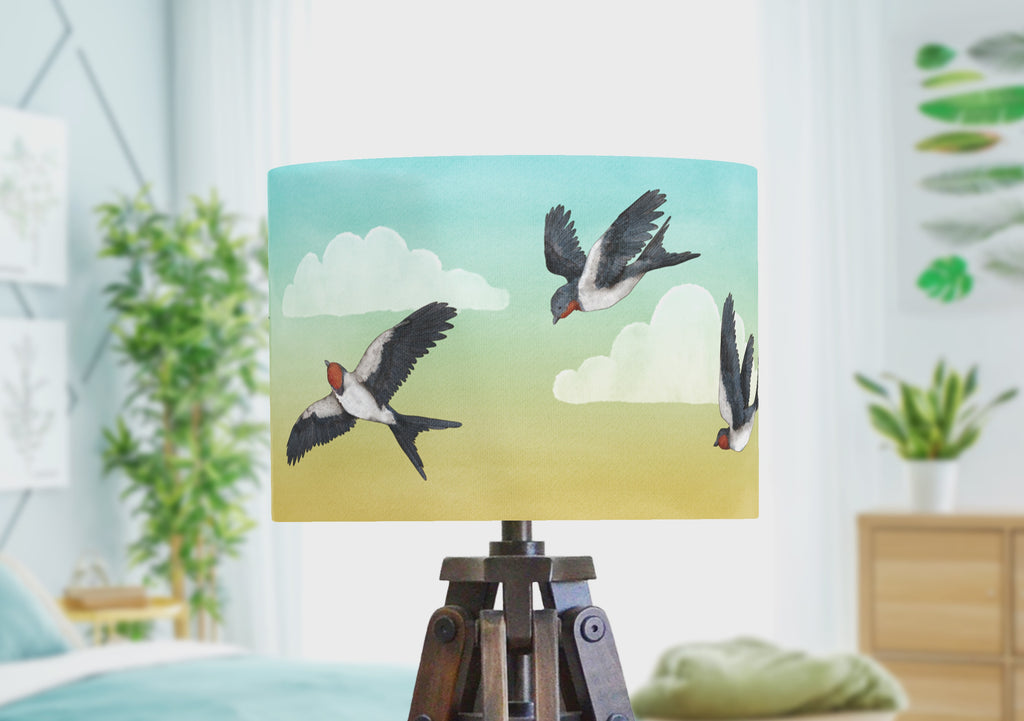 A bird lampshade with swallows flying through a blue and yellow evening sky, rotating to show the full wrap-arround illustration by the artist.