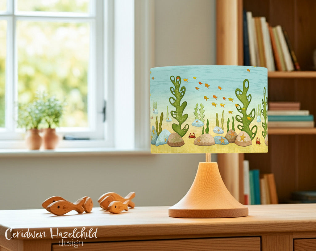 Under The Sea lampshade on an oak lamp base in a bright, cheerful room with wooden decor, styled like a natural children’s reading area.
