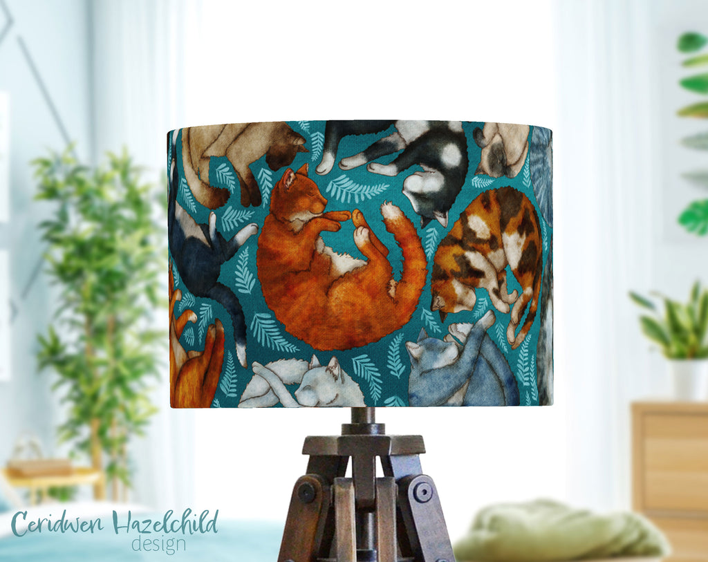 A harbor blue lampshade with illustrations of sleeping cat breeds by Ceridwen Hazelchild
