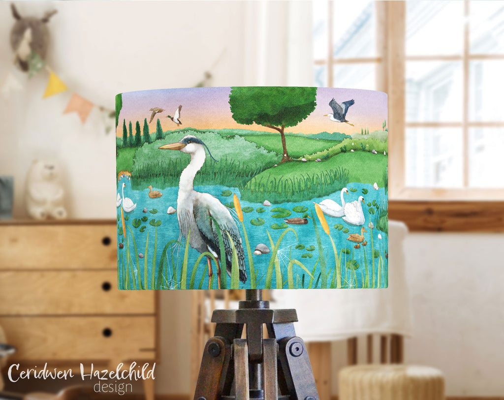 A child's bedroom with a lampshade featuring an illustration of wetland birds in a lake, by Ceridwen Hazelchild.